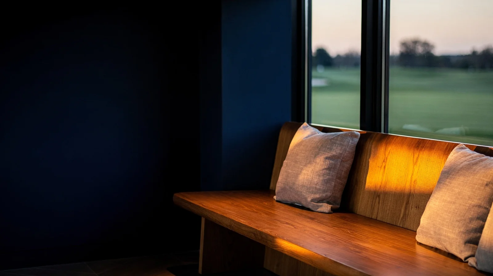 Warm evening light across an oak bench in a quiet clubhouse.